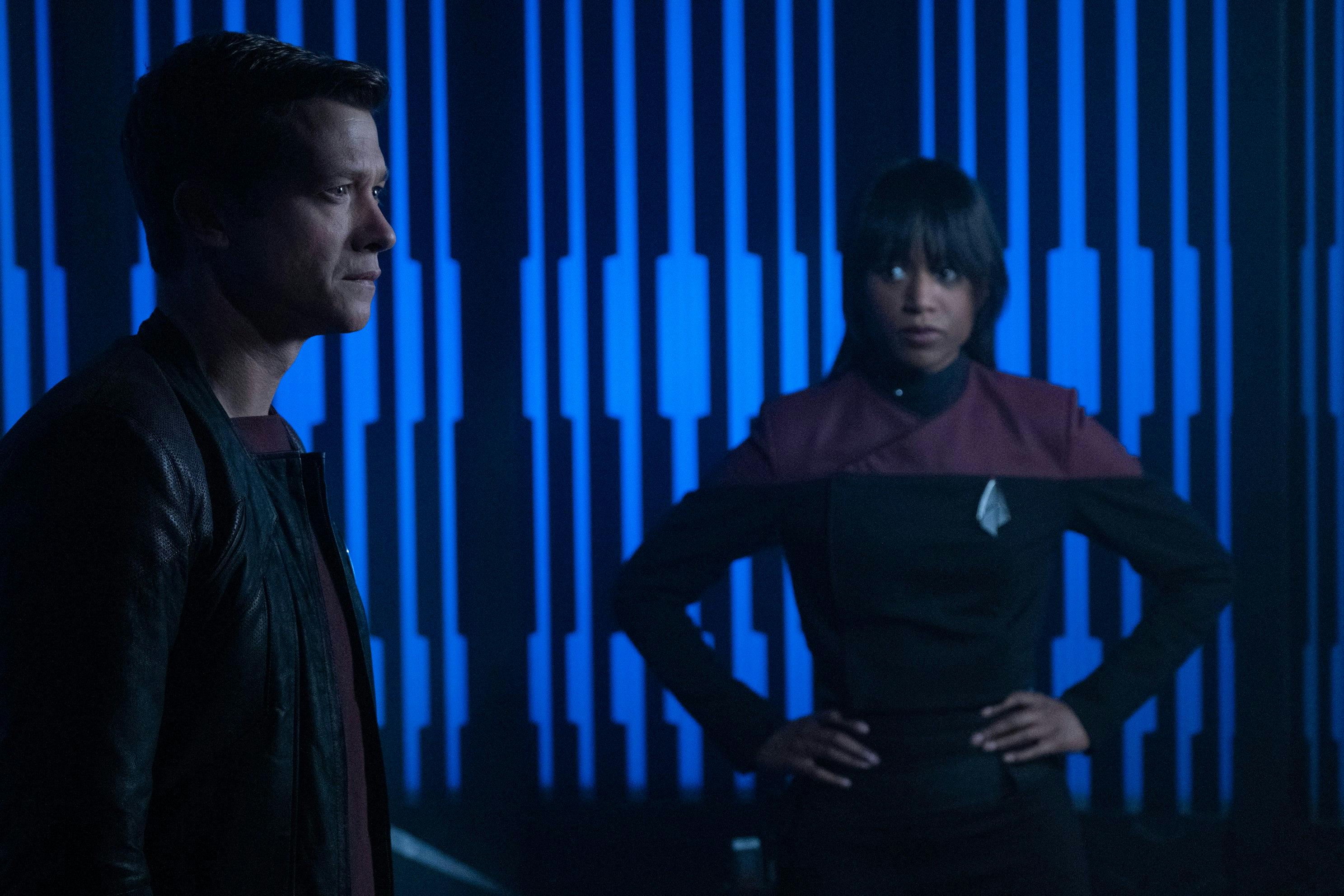 Ensign Sidney La Forge stands with her hands on her hips looking over at Jack Crusher who stares out ahead of him