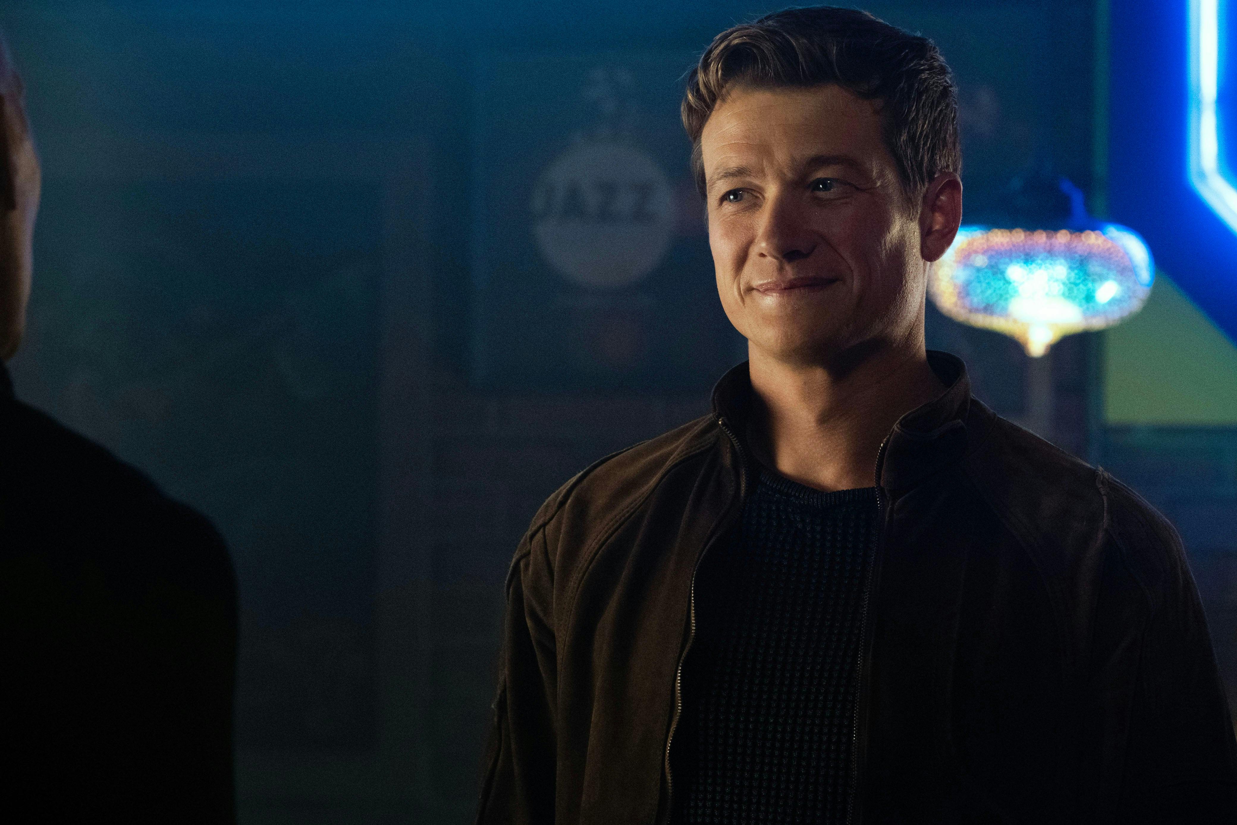 Jack Crusher smiles as he looks to his right at Picard